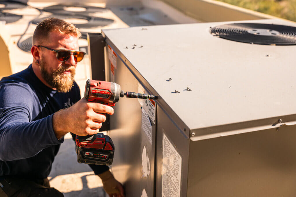 Technician from a leading HVAC companies Tucson homeowners trust performing equipment installation with professional power tools.